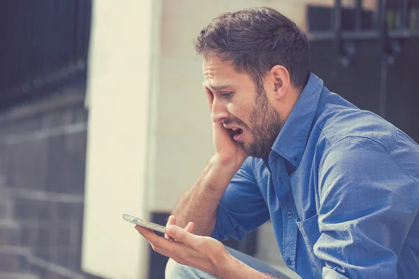 Disperato triste giovane uomo guardando cattivo messaggio di testo sul suo telefono cellulare — Foto Stock