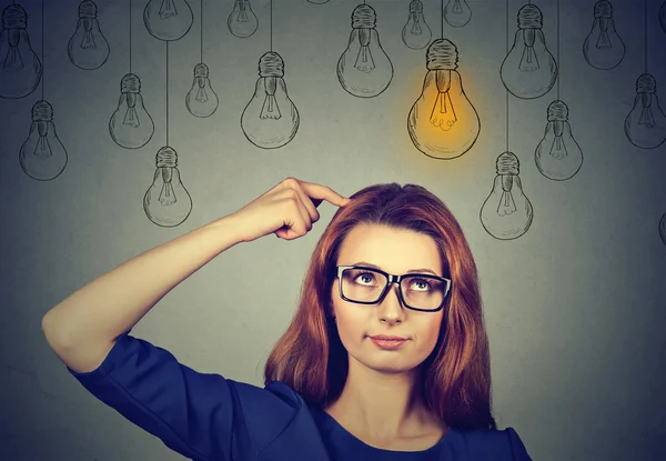 Thinking woman in glasses looking up with light idea bulb above head — 图库照片