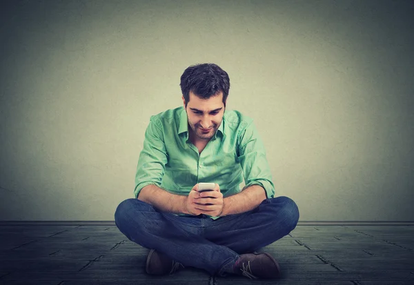 Ευτυχισμένος άνθρωπος χρησιμοποιώντας μηνύματα στο smartphone κάθεται στο πάτωμα του διαμερίσματός του — Φωτογραφία Αρχείου