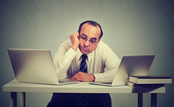 Uomo d'affari annoiato seduto di fronte a due computer portatili — Foto Stock