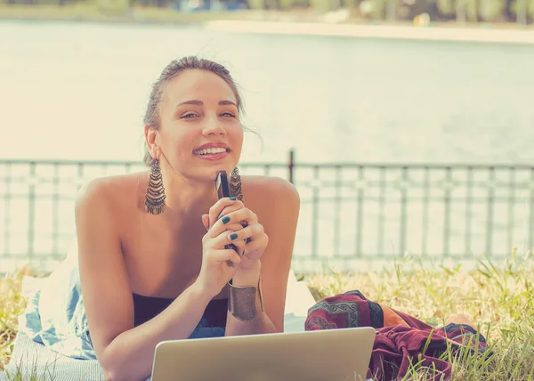 Mujer feliz con ordenador portátil y teléfono móvil relajante en un parque —  Fotos de Stock