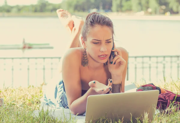 Angry woman talking on mobile phone working on laptop computer outdoors — Stock Photo, Image