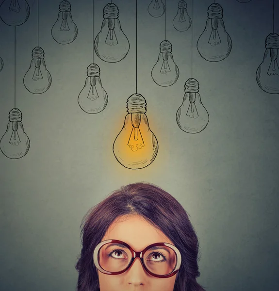 Woman in glasses looking up at light idea bulb above head — Stock Photo, Image