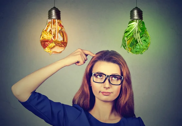 Donna pensando guardando il cibo spazzatura e verdure verdi lampadine — Foto Stock