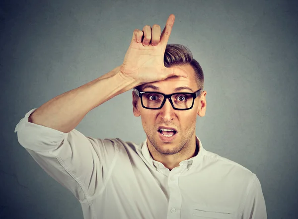 Young man in glasses showing loser sign on forehead — Stockfoto