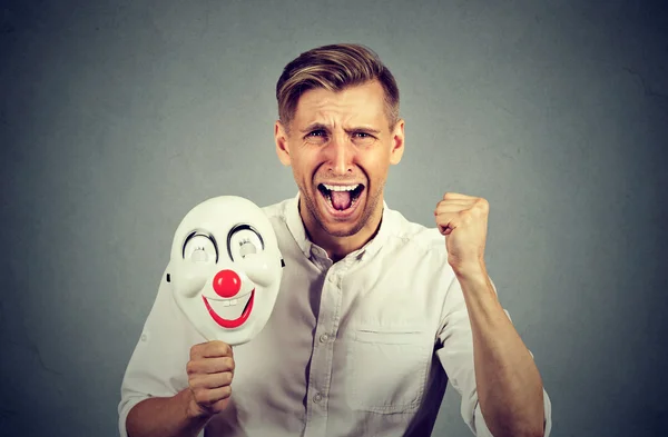 Θυμωμένη ουρλιάζοντας άνθρωπος κρατώντας μάσκα κλόουν εκφράζοντας αγαλλικότητα ευτυχία — Φωτογραφία Αρχείου