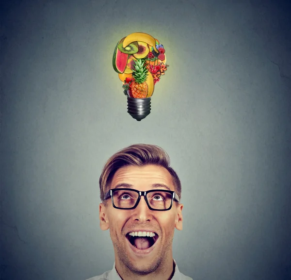 Eating healthy. Man looking up light bulb made of fruits — Stock Photo, Image