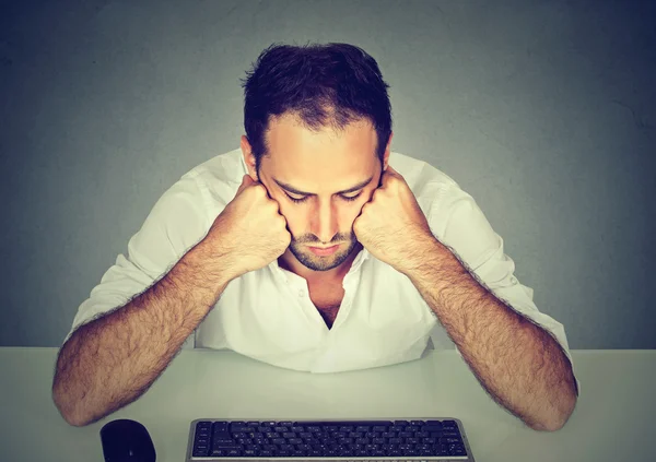 Sad young man sitting at table looking at computer keyboard — Stock Photo, Image