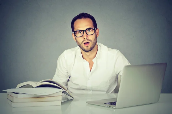 Surprised confused man studying at table with sbooks and laptop