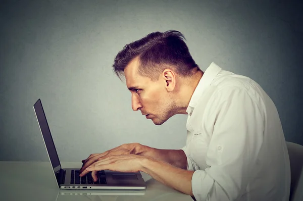 Po stronie profilu młody mężczyzna pracujący na komputerze siedzi przy biurku — Zdjęcie stockowe