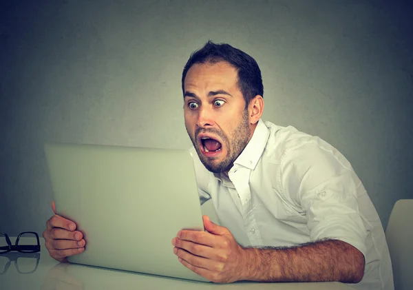 Portret jonge geschokt man met laptopcomputer zitten aan tafel — Stockfoto