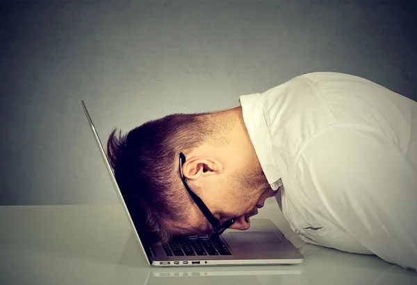Desperat medarbetare betonade ung man vilar huvudet på laptop tangentbord — Stockfoto