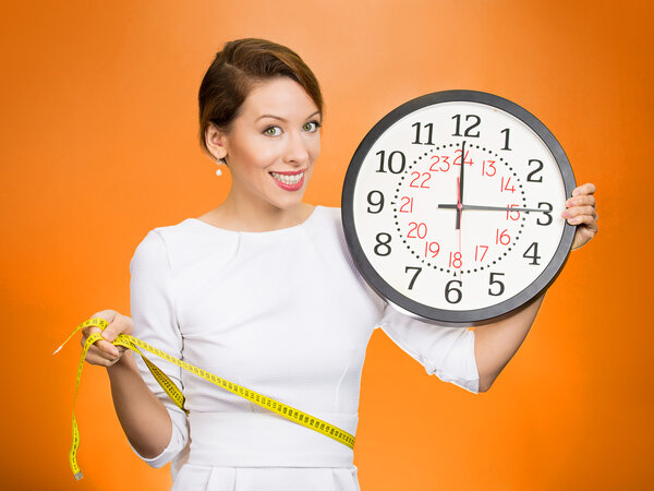 Woman holding clock, measuring her waist with tape