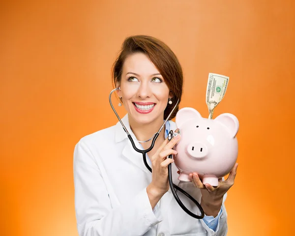 Doctor, nurse listening with stethoscope to piggy bank — Stock Photo, Image