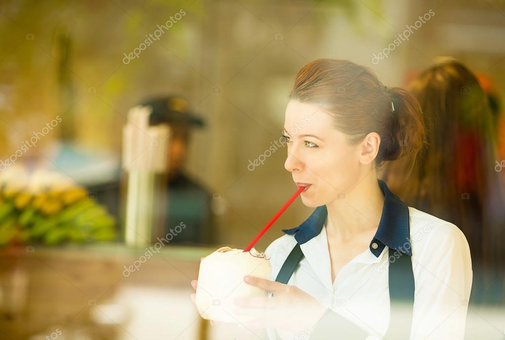 woman drinking coconut juice, looking outside on street through 