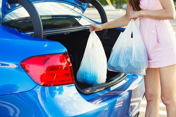 Frau steckt Einkaufstüten in Kofferraum ihres blauen Autos Stockfoto