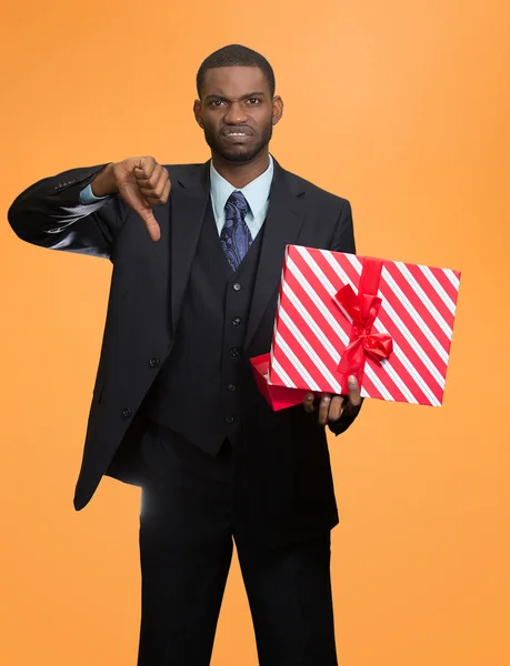 Upset man holding gift box displeased, showing thumbs down — Stock Photo, Image