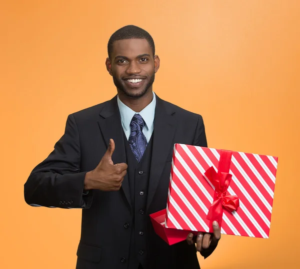 Sorrindo homem de negócios segurando presente, dando polegar para cima — Fotografia de Stock