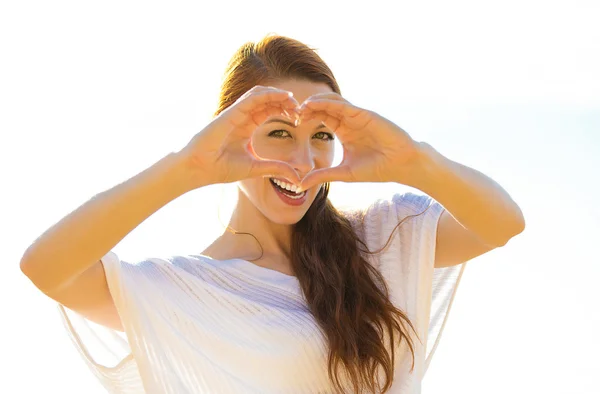 Mooie vrouw toont hart vorm handen op zonnige zomerdag, oceanside achtergrond — Stockfoto