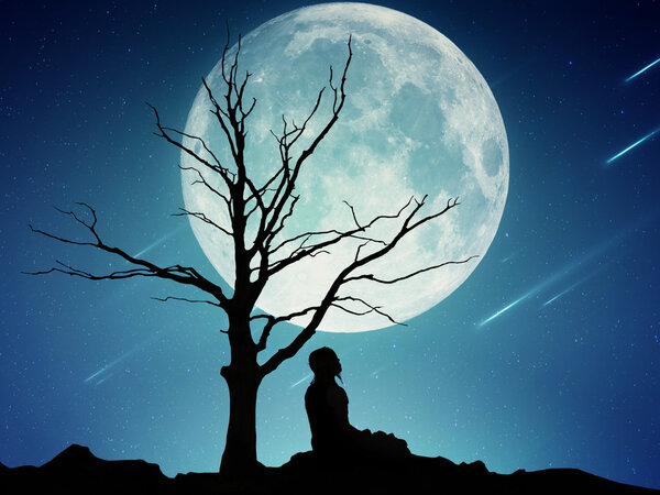 Silhouette of a man sitting under the tree meditating isolated on beautiful background of moon, earth, night skyline, falling stars. Body vitality, human spirit wellbeing concept. Alternative medicine