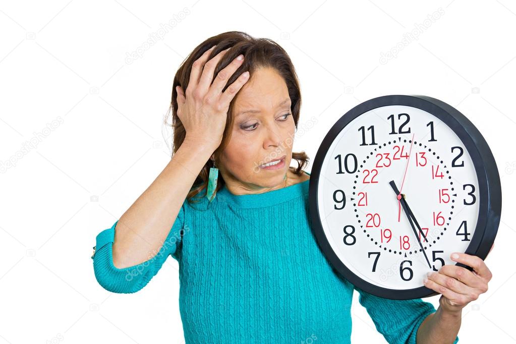 Senior woman holding clock looking anxiously pressured by lack of time