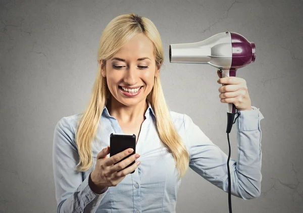 Mujer leyendo noticias en smartphone sosteniendo secador de pelo —  Fotos de Stock