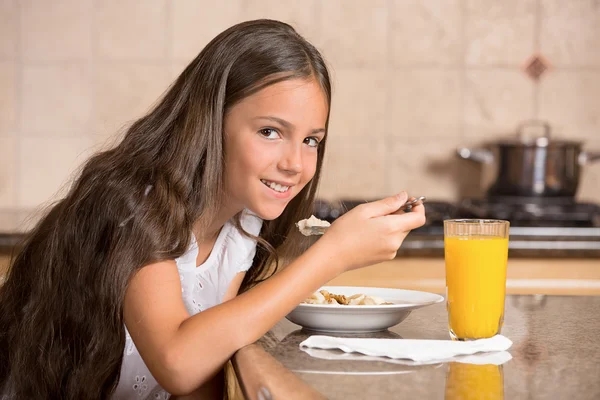 Dziewczynka jedzenie roślin zbożowych z mlekiem do picia sok pomarańczowy na śniadanie — Zdjęcie stockowe