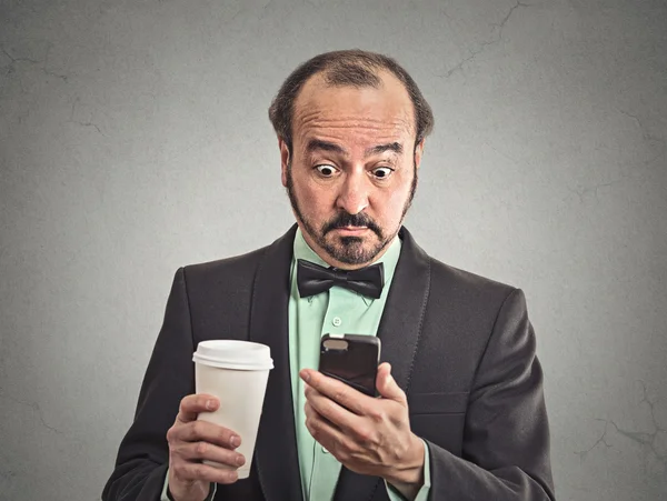 Удивленный мужчина читает новости о том, как смартфон пьет кофе — стоковое фото