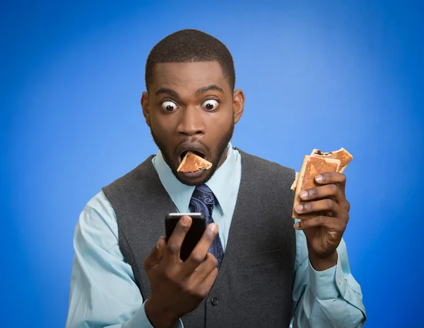 Surprised man using smartphone eating cookie — Stock Photo, Image