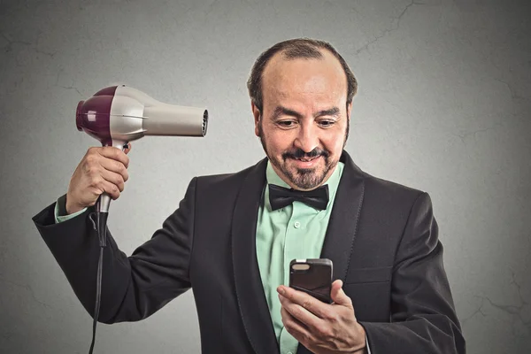 Man reading news on smartphone blowing hair with hairdryer — Stock Photo, Image