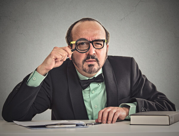 businessman skeptically looking at you through magnifying glass 