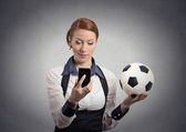 business woman looking on smartphone watching game holding football 