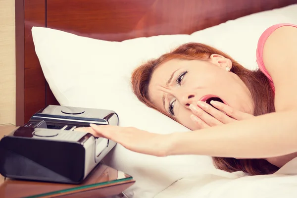 Mujer extendiendo la mano al despertador bostezar se encuentra en la cama —  Fotos de Stock