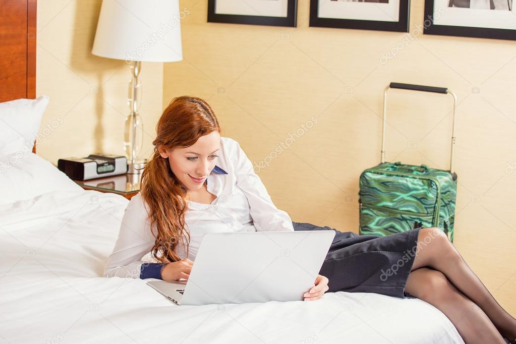 businesswoman working on laptop sitting on the bed in hotel room