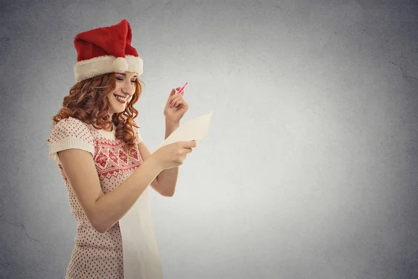 Junges attraktives Mädchen Weihnachtsmann-Helferin mit rotem Hut hält Lesung Weihnachtswunschliste — Stockfoto