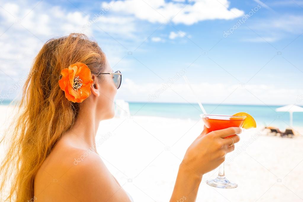 woman in white swimsuit with cocktail on the beach enjoying sunny weather
