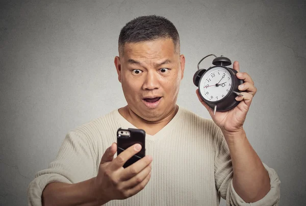 Surprised shocked man with alarm clock looking at smart phone — Stock Photo, Image