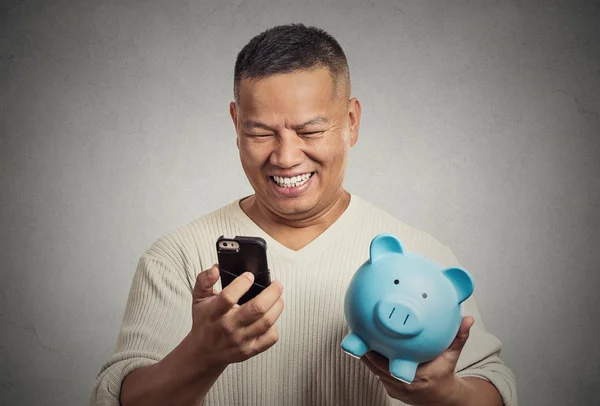 Homem empregado segurando porquinho banco olhando para telefone inteligente — Fotografia de Stock