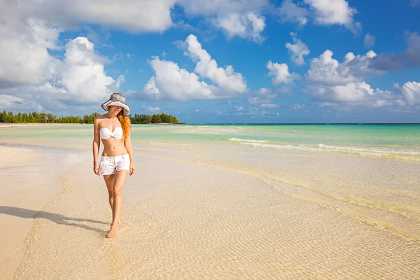 Smiling woman in white shirts and hat walking on beach — Stock Photo, Image