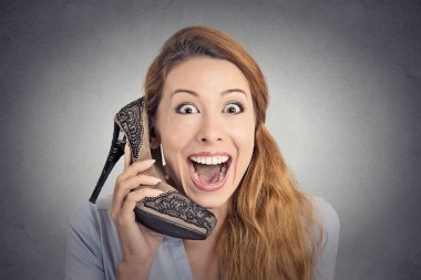 Headshot happy woman looking excited holding high heeled shoe as phone  clipart