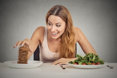 woman deciding whether to eat healthy food or sweet cookies she craving clipart