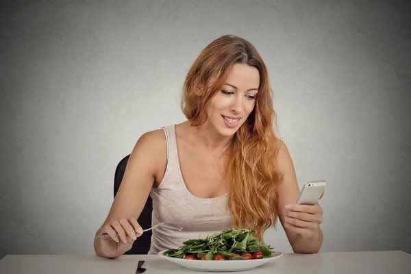 Young woman eating and chatting on mobile phone — Stock Photo, Image