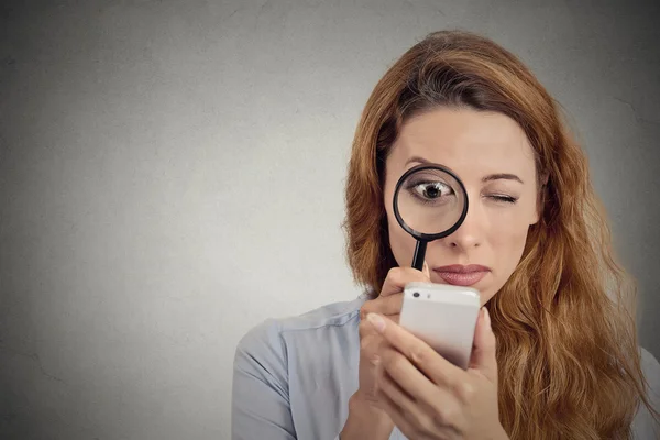 Женщина смотрит через увеличительное стекло на экране смартфона — стоковое фото