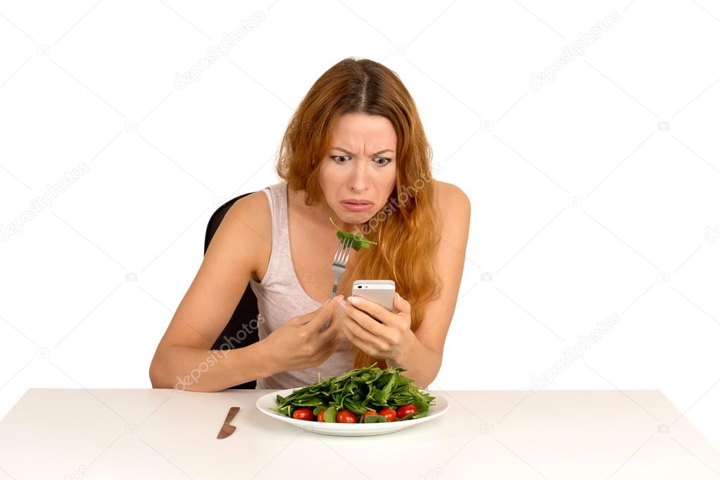 Displeased girl eating green salad looking at phone seeing bad news 