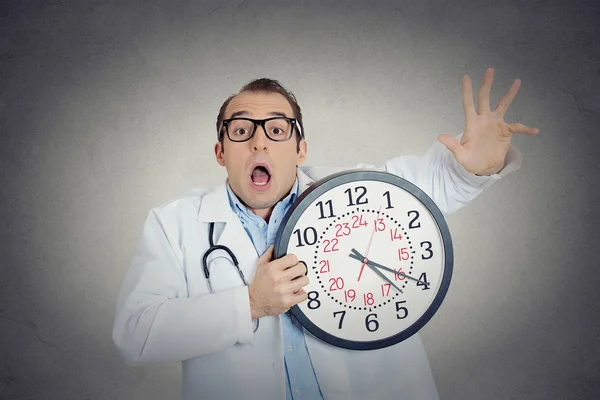 Ocupado, infeliz profissional de saúde masculino, olhar engraçado médico segurando relógio de parede — Fotografia de Stock