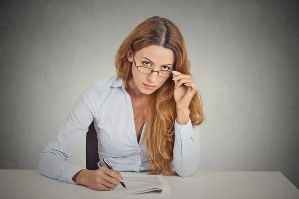 Mujer de negocios con gafas sentada en el escritorio escépticamente mirándote escrutando — Foto de Stock