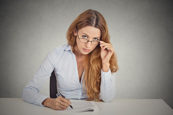 businesswoman with glasses sitting at desk skeptically looking at you scrutinizing