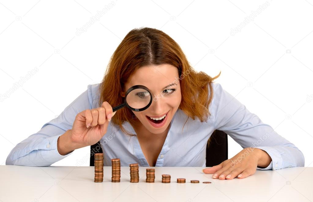 business woman looking at growing stack of coins through magnifying glass