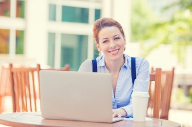 smiling woman working on laptop outside corporate office drinking coffee