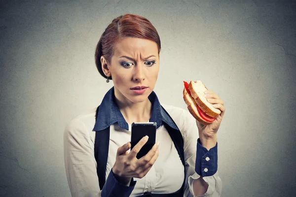 Mujer de negocios mirando su teléfono móvil comiendo sándwich de pan —  Fotos de Stock